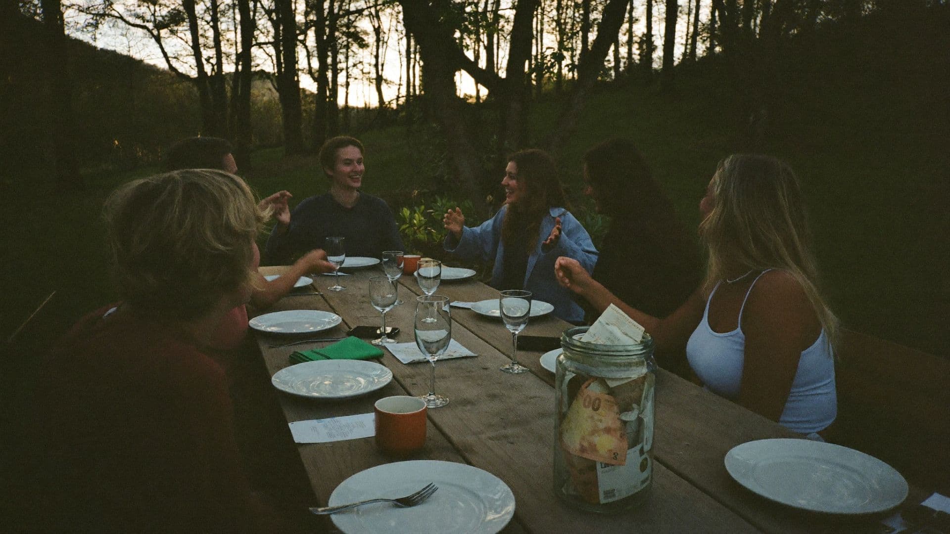 Friends around a table at golden hour, the group's money jar among the plates
